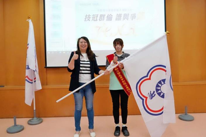 圖1.中彰投分署劉秀貞分署長將代表勝利的旗幟交至誓師代表手中，祝福選手們旗開得勝 _Instructions for literal
